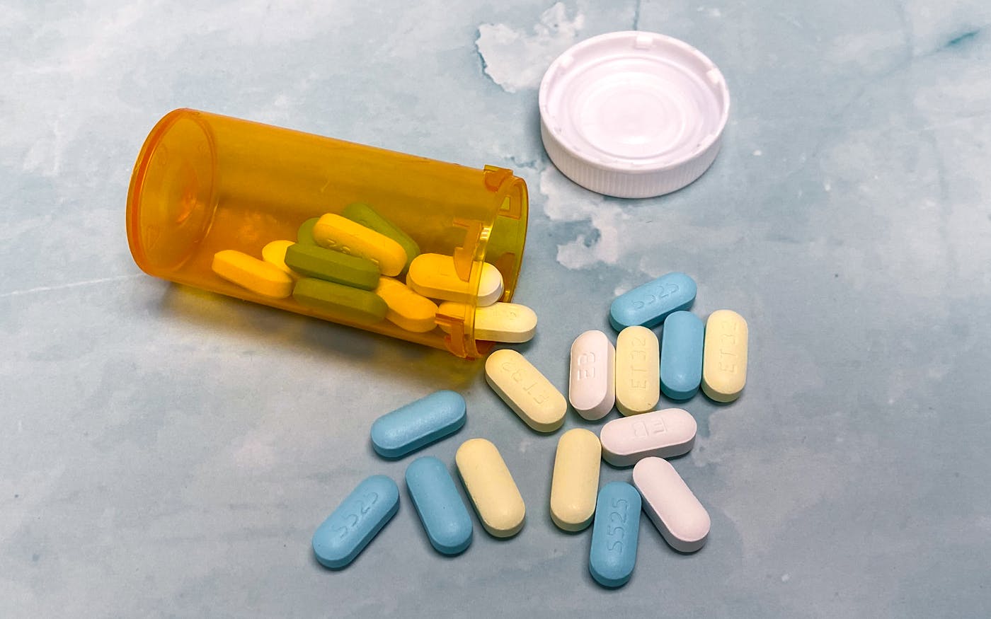 Prescription bottle and assorted tablets on a light blue surface